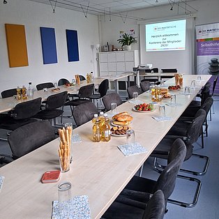 ein langer Tisch mit vielen Stühlen drum herum, auf dem Gläser und Snacks stehen