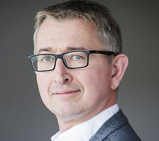 ein Mann mit einer Brille vor einem dunklen Hintergrund