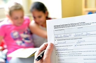 Im Hintergrund 2 Mädchen, vorne hält eine Person einen BuT-Antrag in Händen